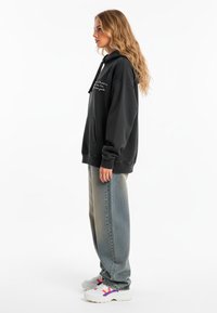 Felpa nera con cappuccio e tasca frontale, con testo bianco. Abbinata a jeans azzurri larghi e sneaker bianche chunky.