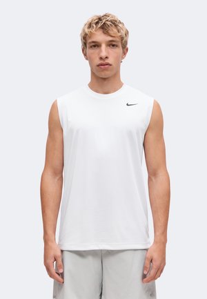 Jeune homme aux cheveux blonds bouclés portant un débardeur de sport blanc avec un petit logo noir Nike sur la poitrine.