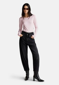 Jasnoróżowa bluzka z długim rękawem w połączeniu z czarnymi dżinsami z wysokim stanem oraz czarnymi botkami na obcasie. Prosty design z luźnym krojem.