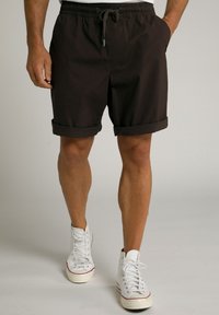 Brune shorts med snor i taljen, opkrøllede manchetter og sidelommer, parret med hvide høj-top sneakers. Glat stofstruktur.