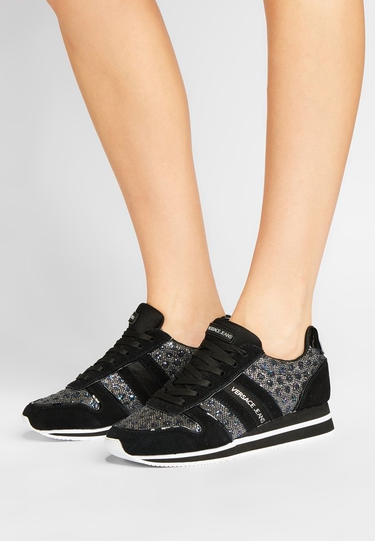 Baskets noires étincelantes avec une tige textile agrémentée d'accent en daim, des lacets noirs et une semelle blanche avec un discret logo sur le côté.