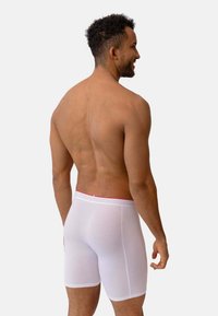 Boxers blancs avec une taille rouge, montrant un ajustement proche et une texture lisse. Le dos du modèle fait face à la caméra sur un fond neutre.