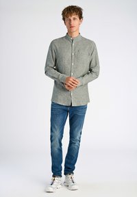 Grijze overhemden met een Mandarin-kraag, lange mouwen en een borstzakje, gecombineerd met blauwe denim jeans en witte sneakers.