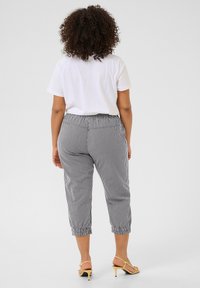 Pantalons cropped rayés en noir et blanc avec une taille élastique et des poignets froncés. Associés à un t-shirt blanc uni et des sandales jaunes.
