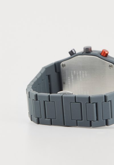 Gray silicone watch with a textured band featuring interlocking links. Metallic back and minimalistic hardware with three colored buttons.