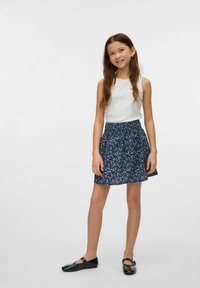 Top sin mangas blanco combinado con una falda de patrón floral azul. La falda tiene una cintura fruncida y cae a mitad del muslo. Zapatos negros completan el conjunto.