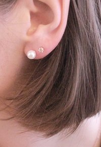 Orecchino a perla e orecchino con piccole cristalli in un lobo, caratterizzati da una forma tonda e una superficie liscia, inseriti in un orecchio forato.