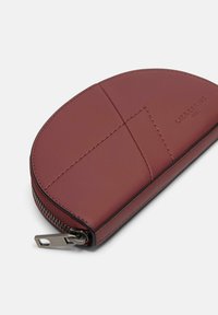 Rote Lederbörse mit abgerundeter Form, Reißverschluss und sichtbaren Nähten. Verfügt über ein strukturiertes Design mit geprägtem Branding.
