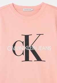 Felpa crewneck rosa con logo "CK" nero e testo "Calvin Klein Jeans" bianco stampato sulla parte anteriore, etichetta di taglia media visibile all'interno del colletto.