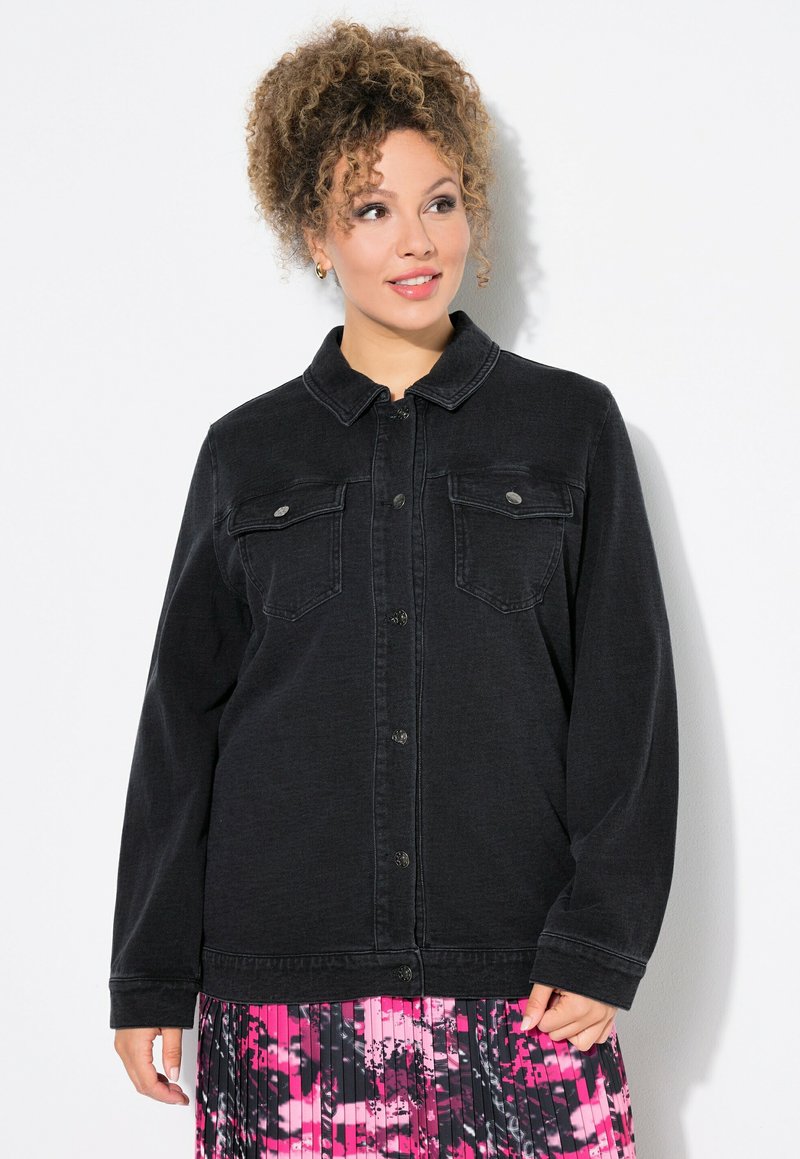 Svart denimjacka med krage, två bröstfickor och knappstängning. Tyget har en lätt struktur som kompletterar en färgglad plisserad kjol.