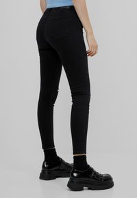 Jeans skinny negros elásticos con talle medio, cinco bolsillos y un ligero desgaste. Combinados con zapatos de plataforma negros gruesos.