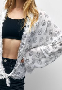 Lekki, biały kimono z czarnymi wzorami liści, z postrzępionymi krawędziami, otwarte z przodu i o luźnym kroju, noszone na czarnym topie crop i szortach dżinsowych.