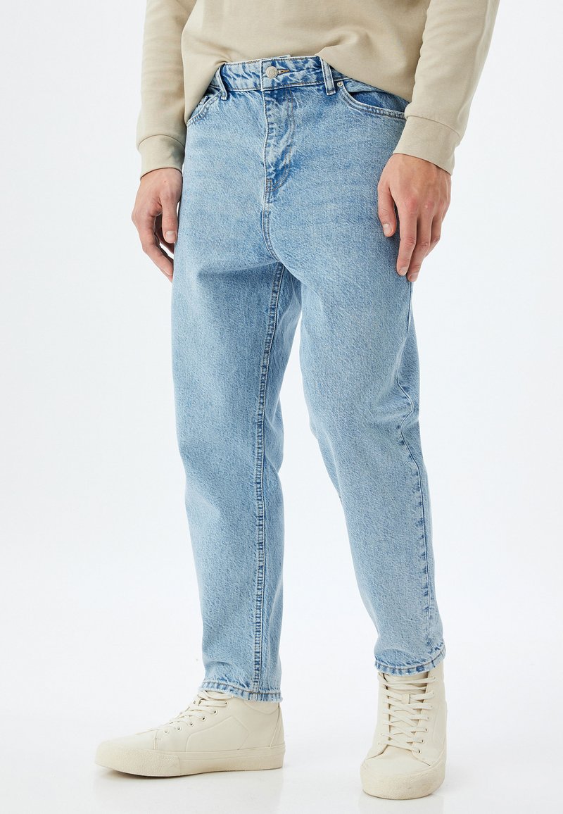 Jeans in denim azzurro chiaro con una vestibilità rilassata, dotati di vita alta, design a cinque tasche e una leggera scoloritura, abbinati a sneakers bianche.