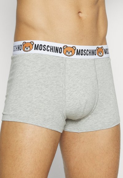 Gaiši pelēki bokseršorti, kas izgatavoti no mīkstas auduma, ar melnbaltu jostu, kurā ir izšūts lācis un zīmola nosaukums "Moschino".