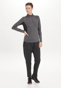 Langærmet grå sports T-shirt med halv lynlås, parret med sorte bukser og teksturerede sorte sneakers med pink detaljer.
