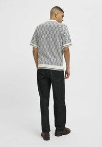 Adīta īsām piedurknēm krekls melnbaltā žakarda rakstā, ar baltu apkakli un ribotām piedurknēm, kombinēts ar tumši ziliem džinsiem.