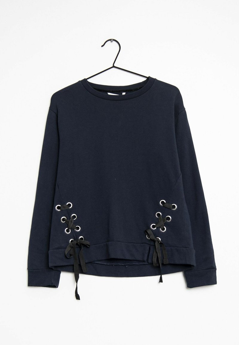 Marinblå sweatshirt hängande på en krok, med snörningsdetaljer med metalöglor på sidorna och svarta satinsnören i nederkant.