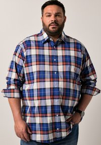 Camicia a quadri blu e bianca con dettagli arancioni, maniche lunghe arrotolate, chiusura con bottoni e colletto. Indossata con jeans scuri e un orologio.