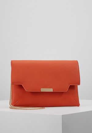 Pochette en cuir orange avec fermoir en métal doré et fine bandoulière chaîne dorée, présentée sur un piédestal blanc sur fond gris.