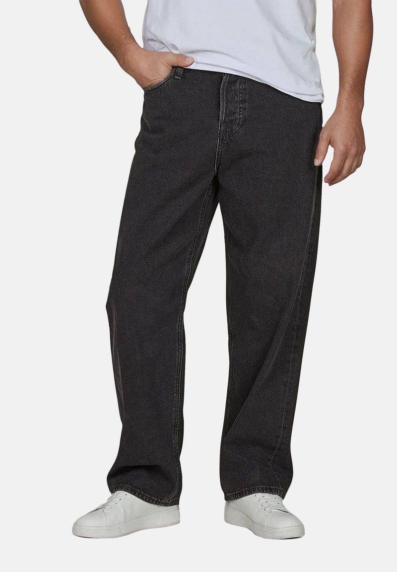 Jeans de denim negro con un ajuste holgado, diseño de cinco bolsillos y sutiles detalles de costura, combinados con zapatillas blancas sobre un fondo neutro.