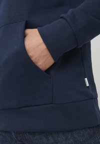 Navy blue sweatshirt featuring a kangaroo pocket, ribbed cuffs, and hem, made from a soft fabric with a smooth texture.