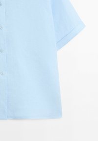 Chemise bleu clair à manches courtes avec boutons devant et poignets de manches pliés, présentée sur un fond blanc.