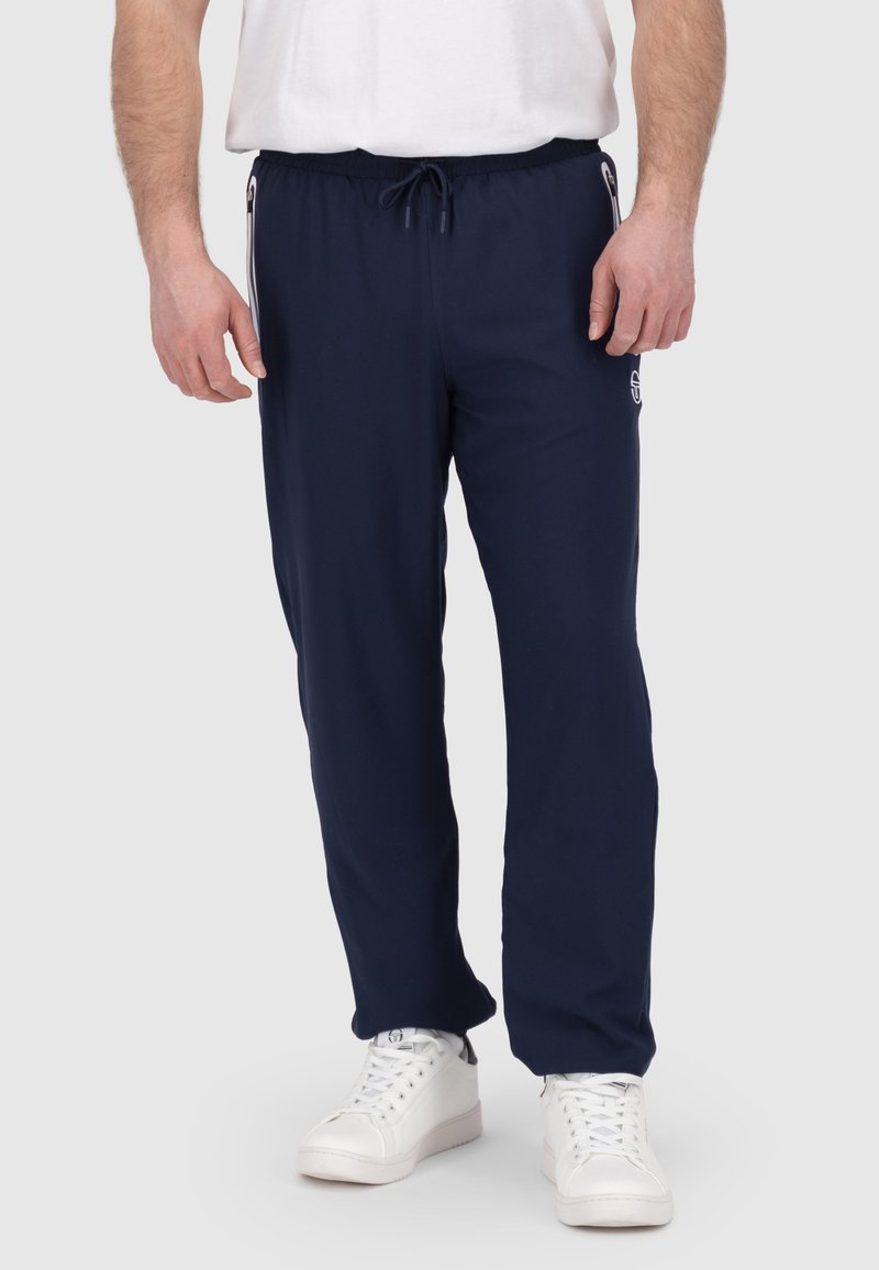 Marineblauwe joggers van zacht materiaal met een trekkoord in de taille, voorzien van zijzakken met rits en een logosticker op de linker dij.