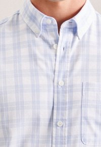Jasnoniebieska i biała koszula w kratkę wykonana z miękkiego materiału, z kołnierzykiem na guziki, guzikami z przodu i kieszenią na piersi.