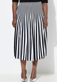 Zwart-wit gestreepte midi rok met een geplooid ontwerp. Glad materiaal en een elastische tailleband, gecombineerd met zilveren hoge hakken.