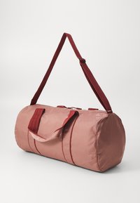 Sac de sport rose brillant avec des accents rouges, de forme cylindrique, avec des poignées doubles et une bandoulière. Il possède une fermeture éclair et des détails cousus.