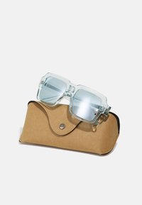 Ochelari de soare pătrați transparenți cu lentile nuanțate de albastru, așezați pe un etui din piele maro cu închidere tip magnet și logo embosat.