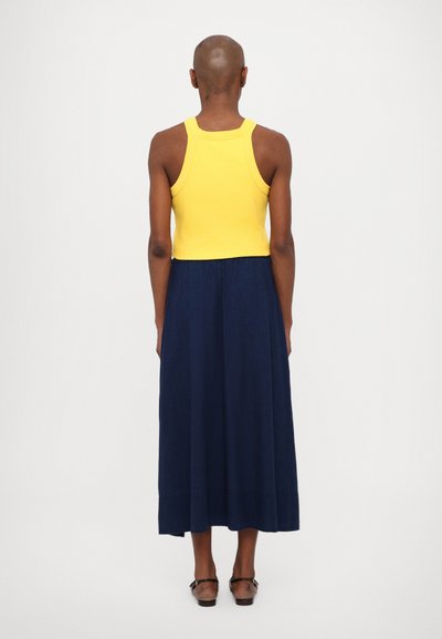 Geel geribbelde tanktop gecombineerd met een lange, vloeiende marineblauwe rok, met een relaxte pasvorm en een gladde textuur, gezien van de achterkant.
