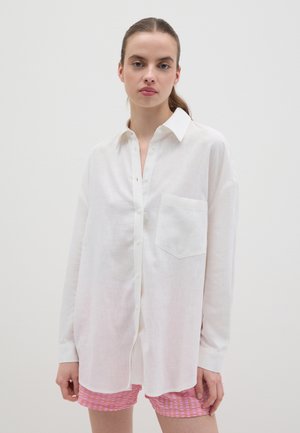 Camisa de botones de manga larga blanca hecha de tejido ligero, con un bolsillo en el lado izquierdo y un corte relajado.