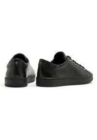 Sneakers in pelle nera con una texture liscia, punta rotonda, suola piatta in gomma e design minimalista. Presentano lacci frontali e unafodera morbida.