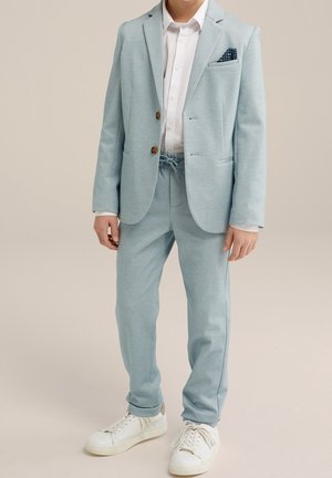 Blazer azzurro chiaro con due bottoni e pantaloni con coulisse abbinati. Completa il look una camicia bianca sotto e sneakers bianche.
