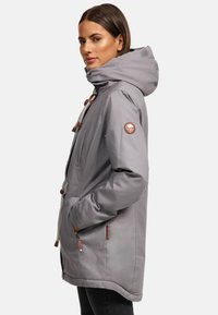 Gray jacket with a high collar and hood, featuring brown leather accents, adjustable drawstrings, and side pockets. Smooth texture.