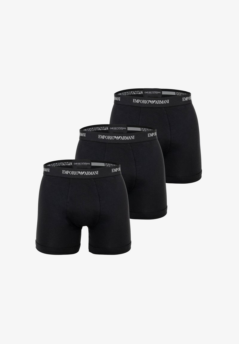 Trois boxers noirs Emporio Armani avec ceintures élastiques à logo, disposés en rangée décalée sur fond blanc.