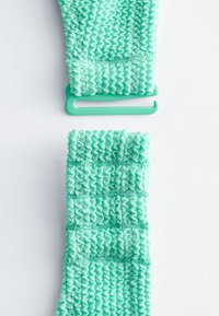 Deux bandes élastiques vertes texturées avec un crochet en plastique, placées verticalement sur une surface blanche.