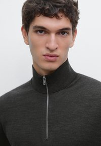 Slim-fit, dark gray zip-up sweater made of soft fabric, featuring a high collar and a silver zipper accent extending to the chin.