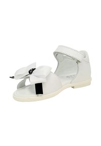 Sandalo bianco per neonato con cinturino alla caviglia e grande fiocco in tessuto sopra la punta aperta su una suola liscia.