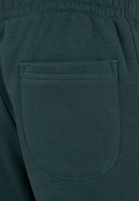 Dunkelgrüne Sweatpants mit einer Gesäßtasche mit abgerundeten Kanten, die mit kontrastierendem Faden genäht ist, und einer weichen Textur. Sichtbarer elastischer Bund.