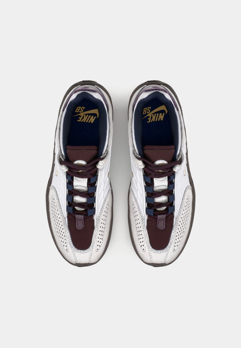 Baskets Nike SB avec une tige en mesh blanc et textile violet, langue rembourrée et lacets plats bleu marine et bordeaux. Semelle extérieure texturée pour l'adhérence.