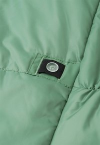 Pikowana kurtka w miękkim zielonym materiale o gładkiej fakturze. Posiada czarny zatrzask i wzmocnione szwy.
