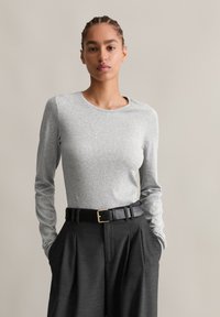 Világosszürke, hosszú ujjú póló kerek dekoltárral, magas derekú sötét nadrággal és fekete bőr övvel, arany csattal párosítva.