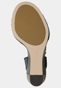 Semelle de chaussure en cuir noir avec une base en caoutchouc texturé. Le talon présente un accent beige et un logo gravé. Forme plate et arrondie.