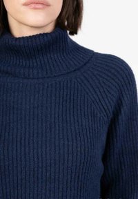 Pull à col roulé en tricot côtelé bleu marine avec une finition texturée et une coupe ajustée, présentant un col haut et un design de manches raglan.