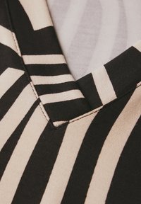 Svart och krämfärgad randig tyg med V-ringning. Texturen verkar mjuk med kontrasterande färgband och synliga söm detaljer.