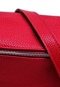 Rode leren handtas met een gestructureerd oppervlak, een opvallende ritssluiting en een platte, verstelbare schouderband. De vorm is rechthoekig.