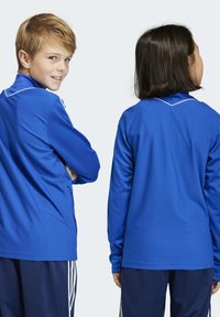 Blaue Sportshirts aus strapazierfähigem Stoff mit weißen Akzenten. Das Design hat lange Ärmel und einen runden Halsauschnitt und wird von zwei Kindern getragen.