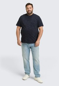 Marineblaue melierte T-Shirt mit Tasche, kombiniert mit hellblauen Jeans und weißen Sneakern; lässiger Schnitt und glatte Baumwolltextur.